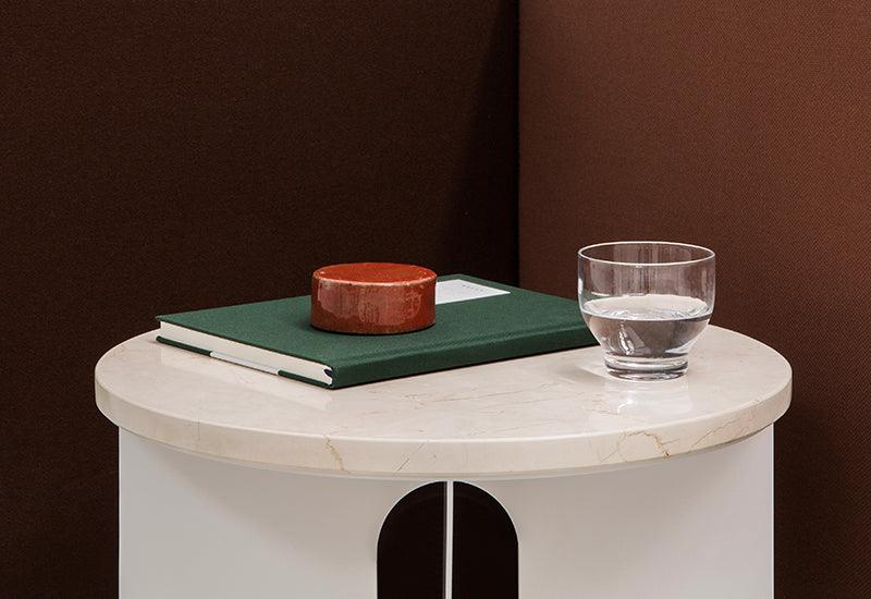 The Androgyne Side Table by Danielle Siggerud for Audo Copenhagen in ivory with crystal rose table top with book placed on its surface.
