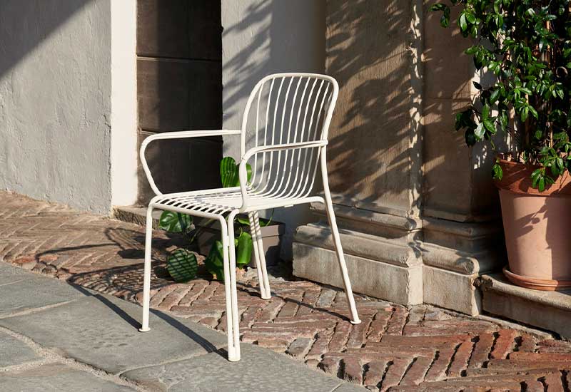 A single ivory Thorvald Armchair by Space Copenhagen for &tradition positioned outside.