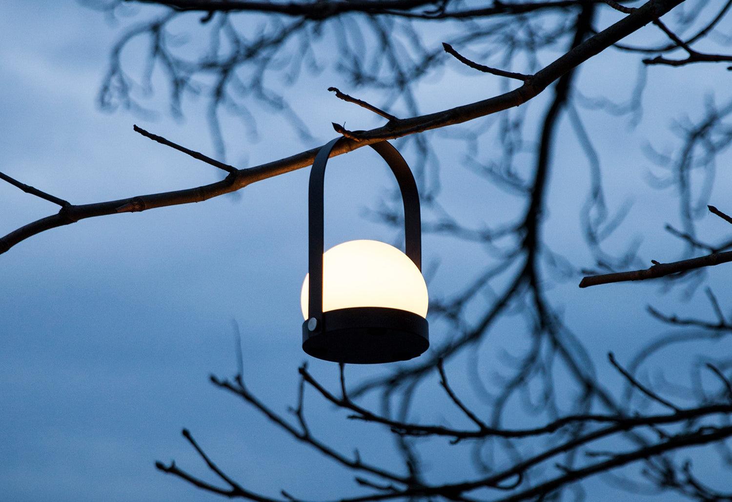  The The Carrie Portable Lamp by Norm Architects for Audo Copenhagen in black hung in a tree.