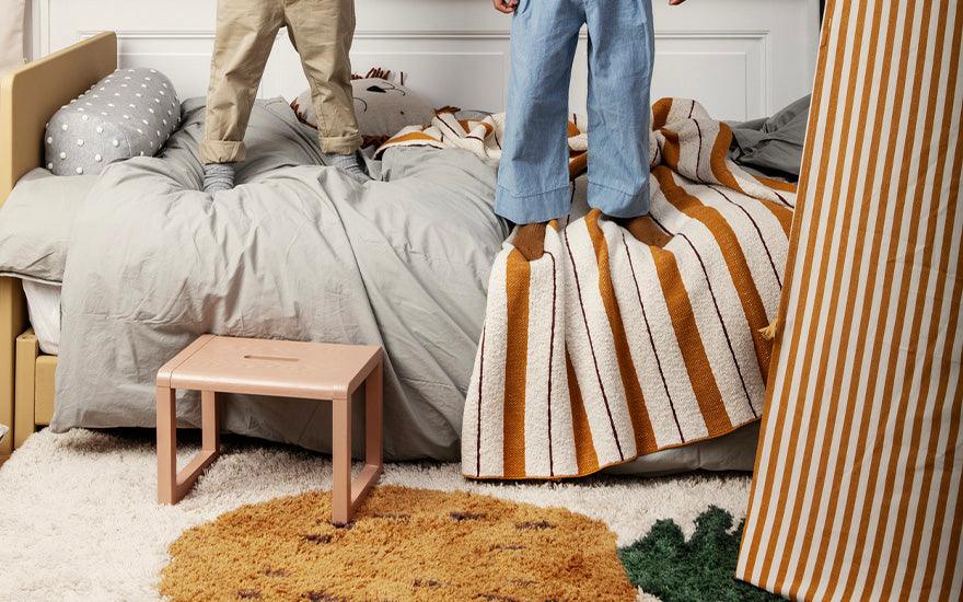  A rose coloured Little Architect Stool sat next to a child's bed.