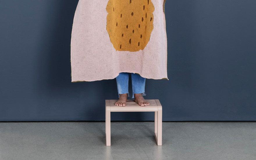 A child stands on a rose coloured Little Architect Stool. The stool is designed by Ferm Living.