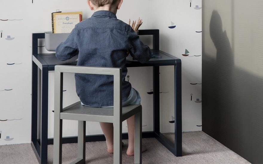 A child sits at a Ferm Living Little Architect Desk in dark blue.