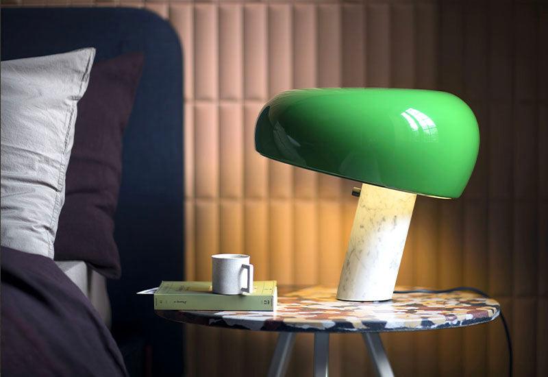 The Snoopy table lamp by A Castiglioni & P.G Castiglioni for Flos with a green glass shade and a white marble base. Placed on a side table.