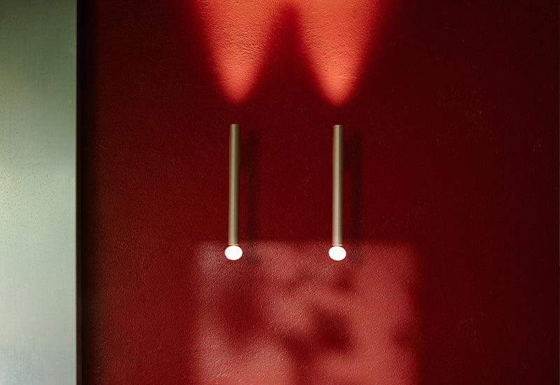  Two copper Flauta Indoors light with lower reflectors displayed on a  red wall. Designed by Patricia Urquiola for Flos.