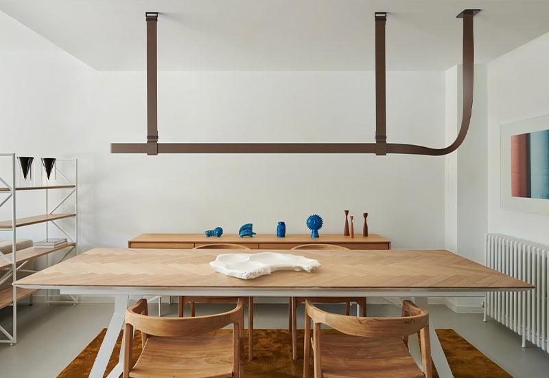  Designed by Ronan and Erwan Bouroullec, the Belt suspension light in natural leather hangs above a wooden table.