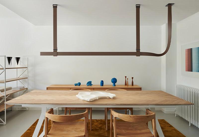 Designed by Ronan and Erwan Bouroullec, the Belt suspension light in natural leather hangs above a wooden table.