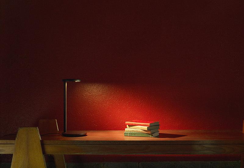 The Oblique lamp, by Vincent van Duysen for Flos, black. The lamp is switched on and placed at a desk.