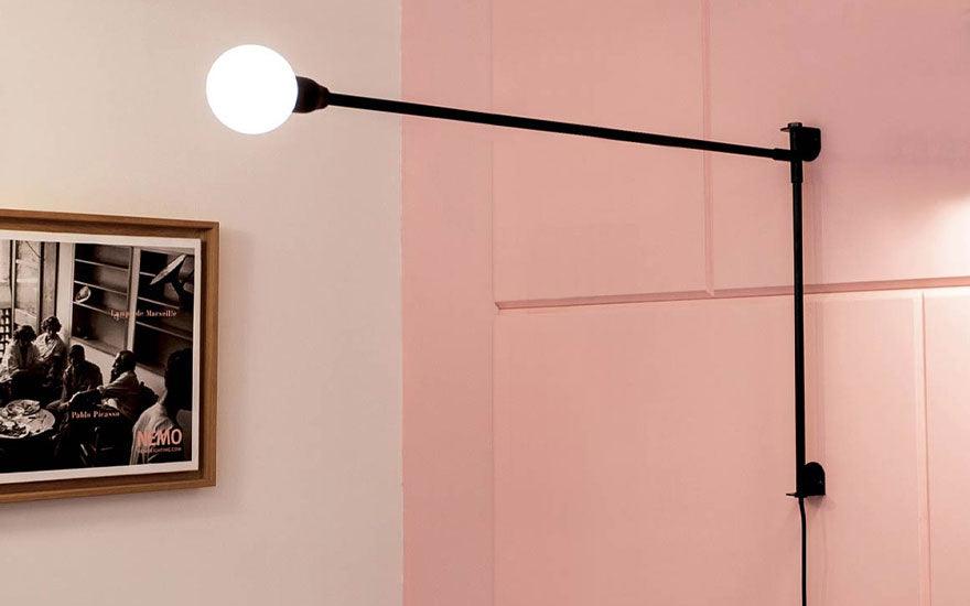 The Mini Potence Pivotante by Charlotte Perriand for Nemo Lighting on a pink wall, next to a framed poster.