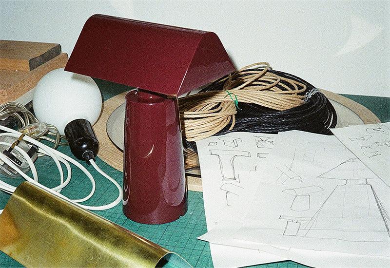 The Caret portable light by Mateo Fogale for &tradition in dark burgundy with sketches of the light.