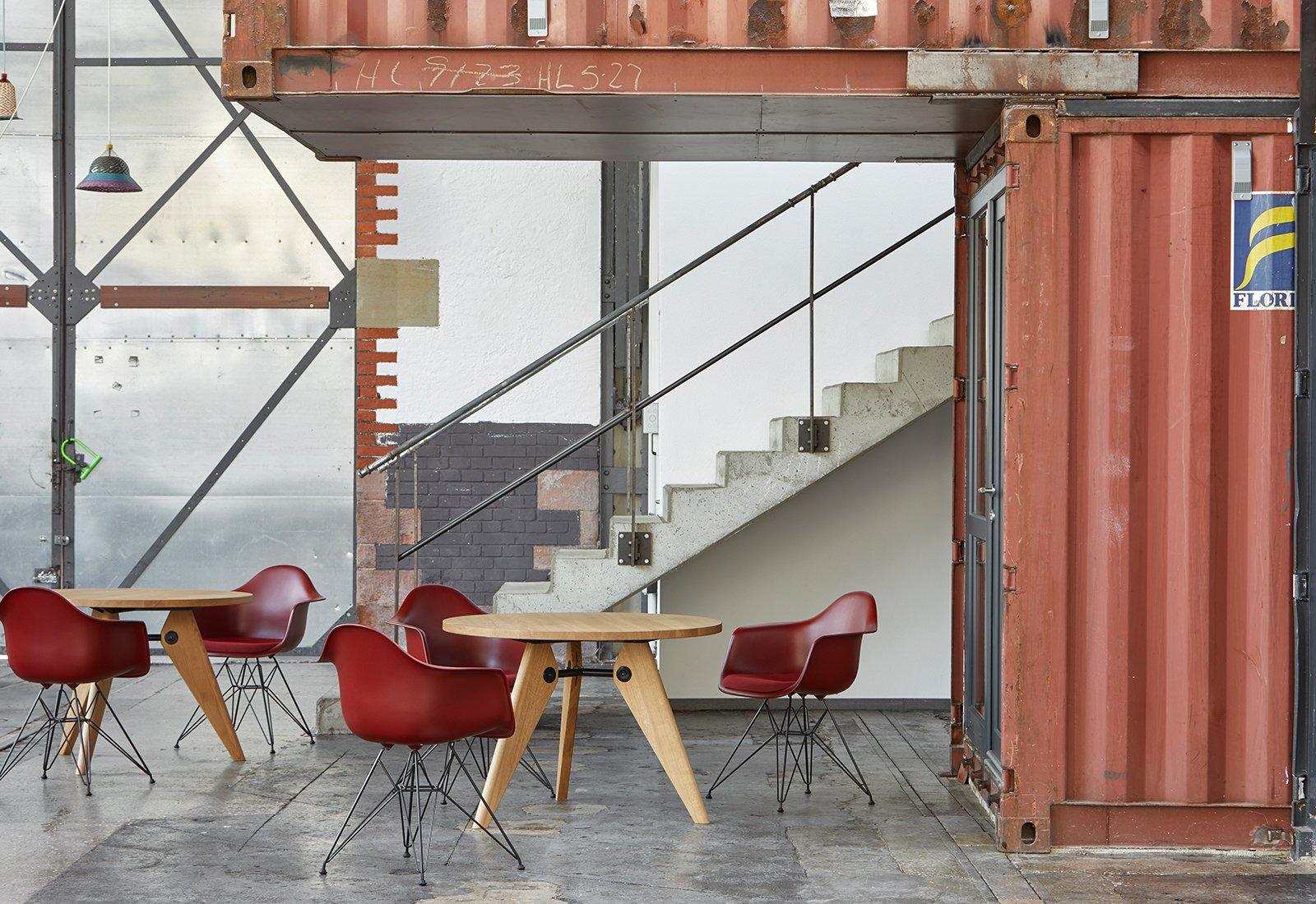 A collection of red Eames DAR Armchair by Charles + Ray Eames for Vitra around wooden tables.