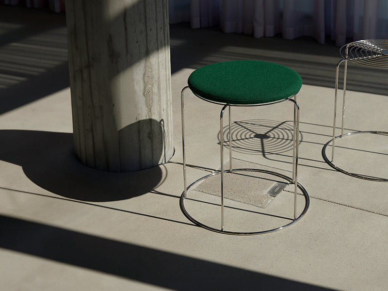  A Wire Stool with green cushion in a room with column. Lots of light is pouring in creating dramatic shadows.