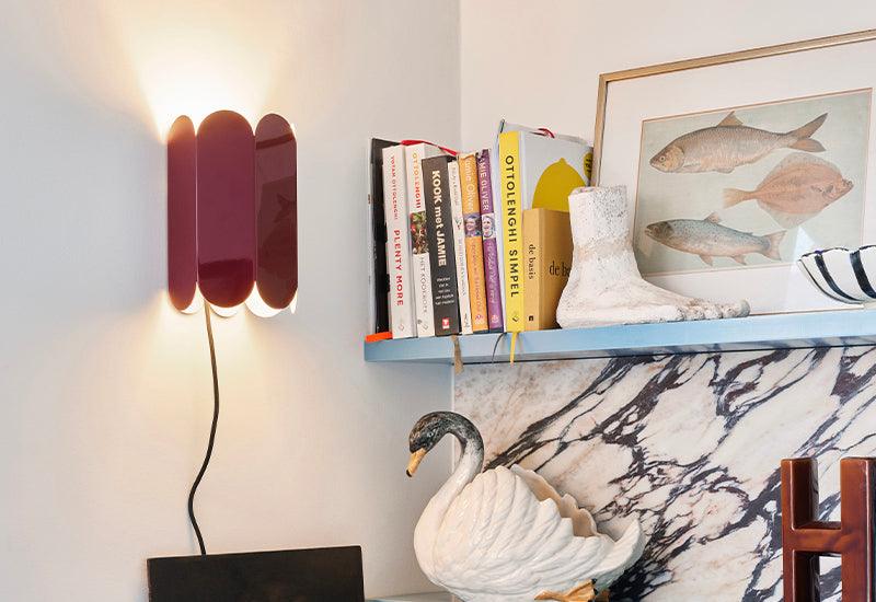  Designed by Muller Van Severen for HAY, the Arcs wall light in auburn red displayed next to a shelf.