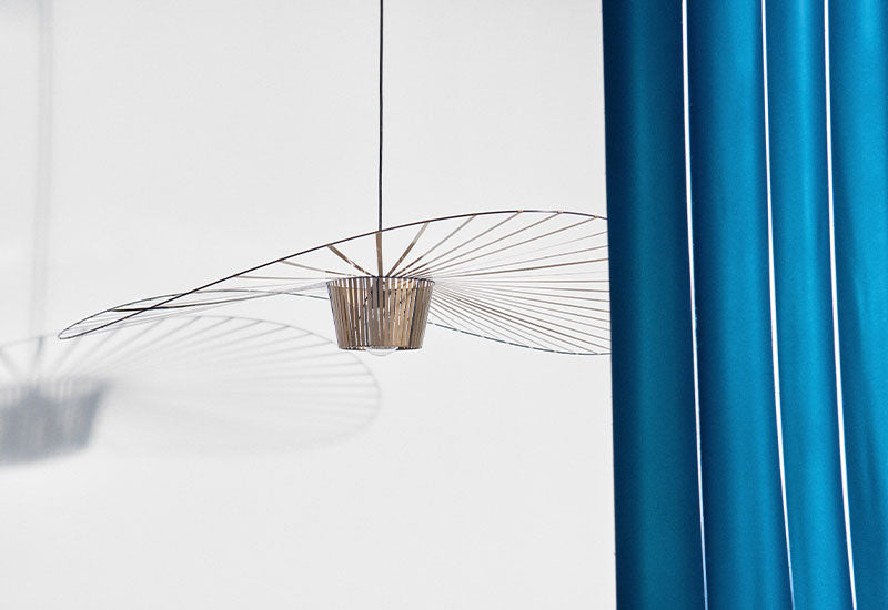  The Bronze Vertigo pendant light by Constance Guisset for Petite Friture peeking out from behind a blue curtain.