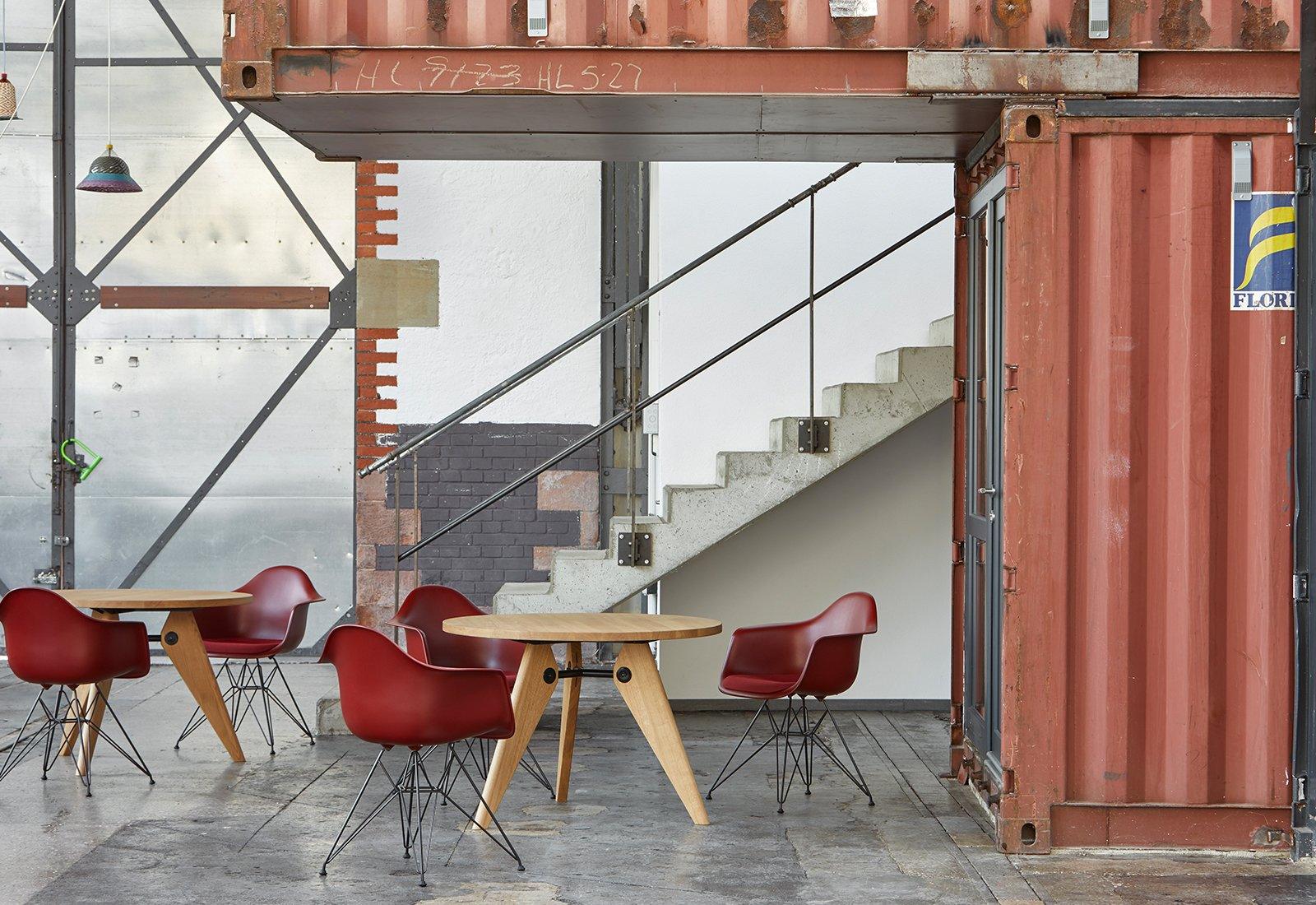  A collection of red Eames DAR Armchair by Charles + Ray Eames for Vitra around wooden tables.